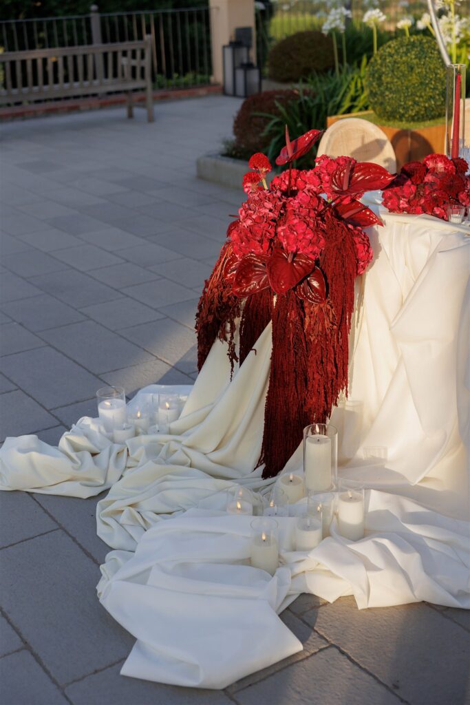 An Unforgettable Anniversary at Castello del Nero: A Three-Day Celebration in Tuscany 31 Elegant red floral arrangement with white draped fabric and candles on a patio. Anniversary Castello del Nero - Italian Wedding Designer