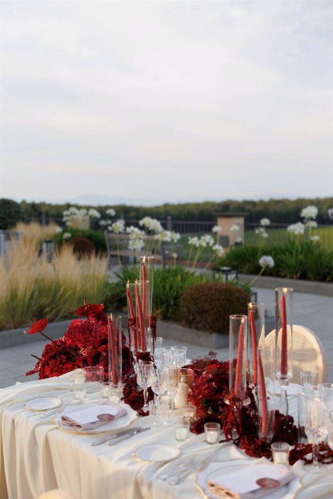 An Unforgettable Anniversary at Castello del Nero: A Three-Day Celebration in Tuscany 32 Elegant wedding reception table setting with red floral arrangements and tall candles outdoors. Anniversary Castello del Nero - Italian Wedding Designer