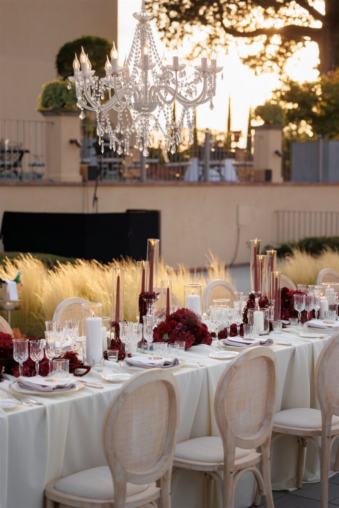 An Unforgettable Anniversary at Castello del Nero: A Three-Day Celebration in Tuscany 44 Elegant outdoor wedding reception table setting with crystal chandelier and red floral accents. Anniversary at Castello del Nero - Italian Wedding Designer