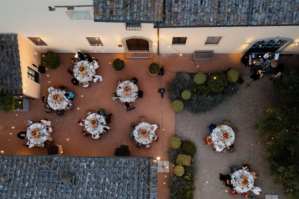 An Unforgettable Anniversary at Castello del Nero: A Three-Day Celebration in Tuscany 19 Aerial view of an outdoor wedding reception with round tables and string lights. Anniversary Castello del Nero - Italian Wedding Designer