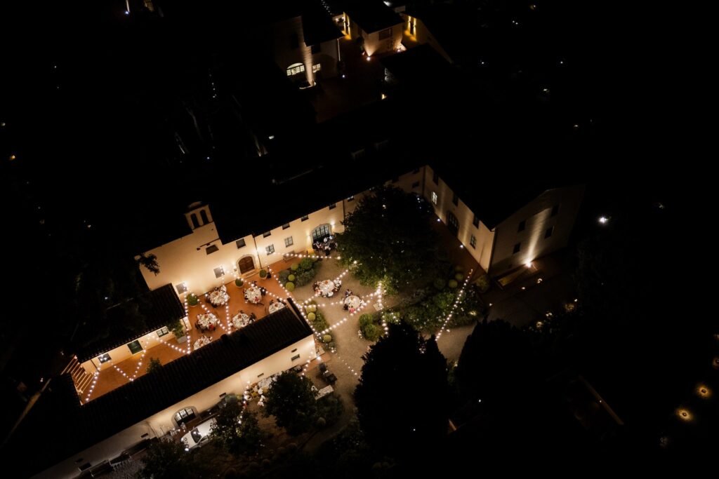An Unforgettable Anniversary at Castello del Nero: A Three-Day Celebration in Tuscany 22 Aerial view of a Tuscan wedding venue at night with romantic string lights and tables set for guests. Anniversary at Castello del Nero - Italian Wedding Designer