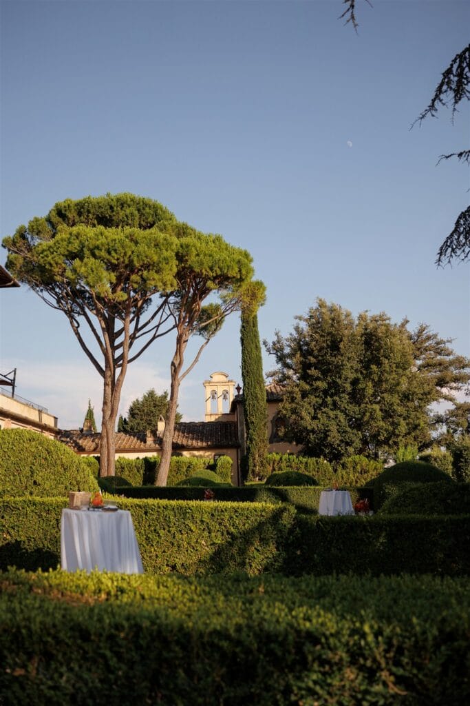 An Unforgettable Anniversary at Castello del Nero: A Three-Day Celebration in Tuscany 3 Formal Italian garden with manicured hedges, trees, and two draped tables. Italian Wedding Designer