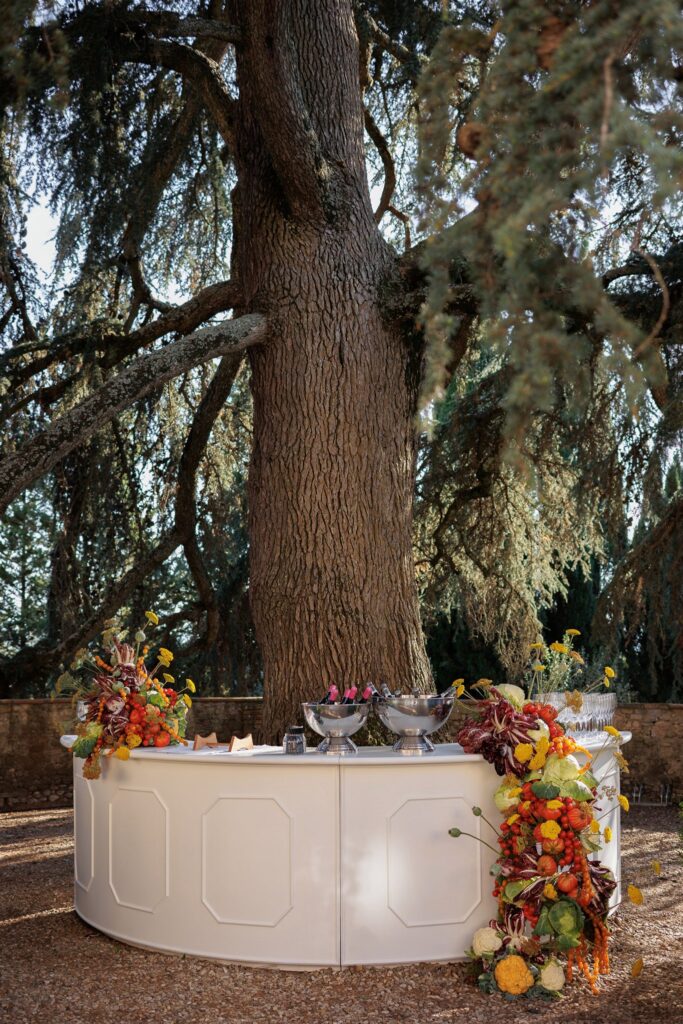 An Unforgettable Anniversary at Castello del Nero: A Three-Day Celebration in Tuscany 8 White wedding bar with vibrant autumn floral decor under a large tree